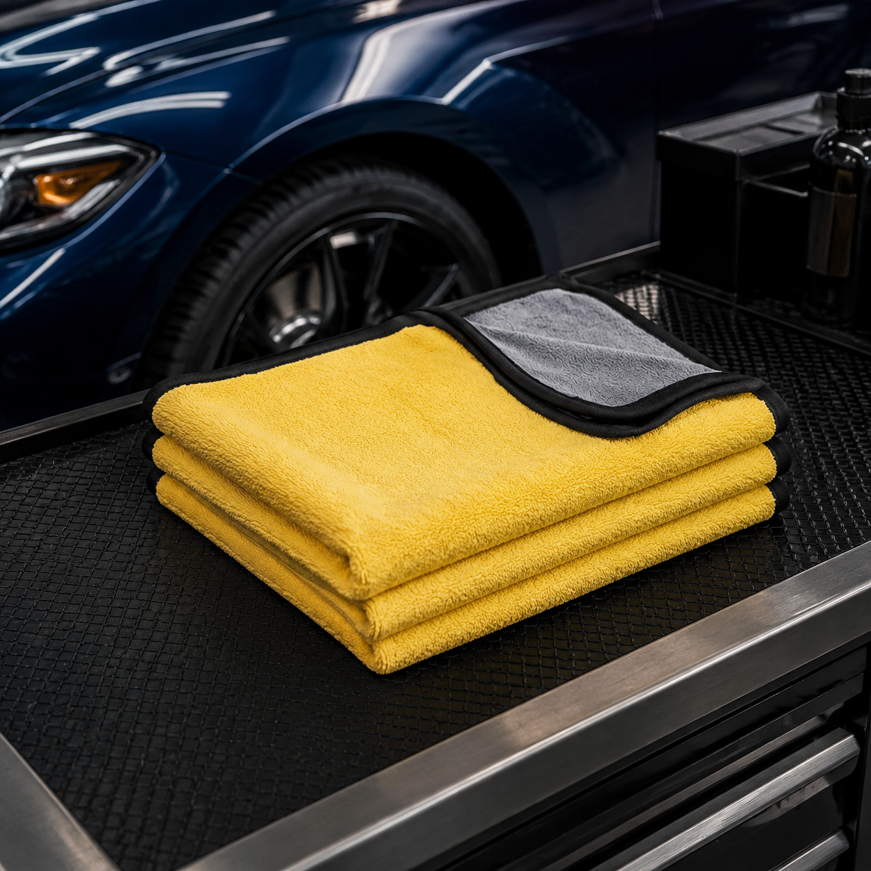Three 30 by 60 cm yellow and charcoal microfiber car towels on a detailing bench