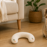 White U-shaped plush pet pillow beside a curious cat in a warm living room