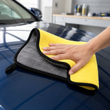 Yellow and charcoal microfiber detailing towel wiping a dark blue car hood