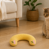 Yellow U-shaped plush pet pillow beside a curious cat in a warm living room